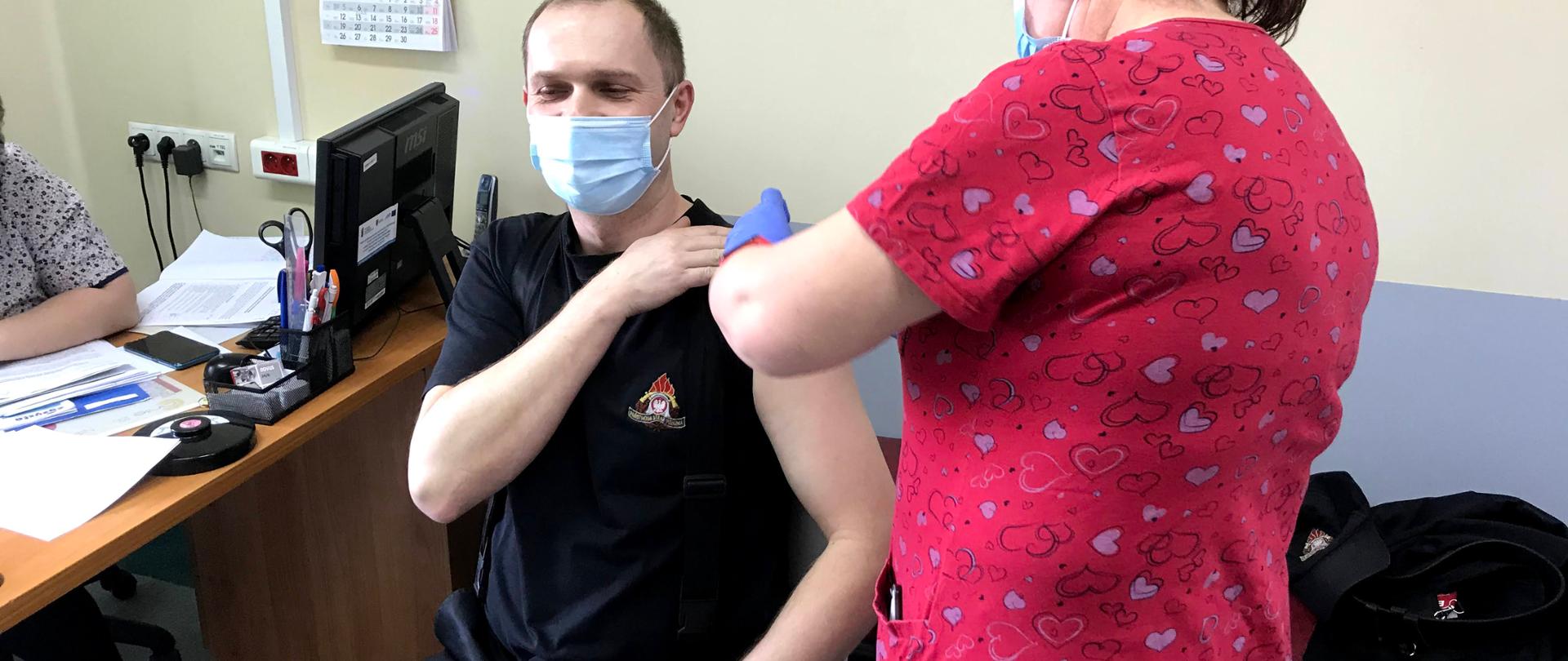 Strażak siedzi pani pielęgniarka dokonuje szczepienia