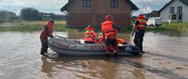 Na zdjęciu widzimy zalaną drogę i strażaków którzy przy wykorzystaniu pontonu prowadzą ewakuację. 