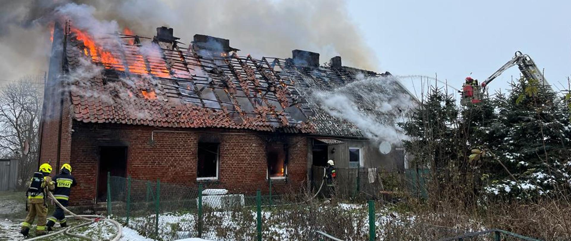 Strażacy w trakcie działań gaśniczych na zewnątrz budynku. 