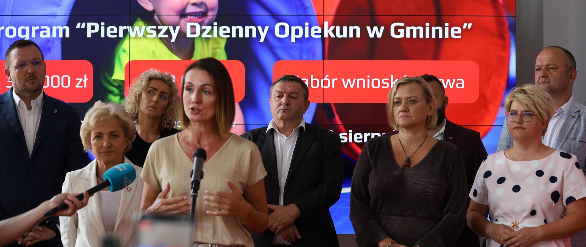 kilka osób stoi na tle banneru z napisem Pierwszy dzienny opiekun w gminie