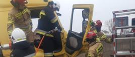 Warsztaty z zakresu ratownictwa technicznego. Złomowisko w Chojnie. Strażacy, którzy wykonują dostęp do poszkodowanego znajdującego się w kabinie ciężarówki. Jeden z dwóch strażaków znajdujących się na podeście operuje narzędziami hydraulicznymi, dwóch innych przytrzymuje drzwi.