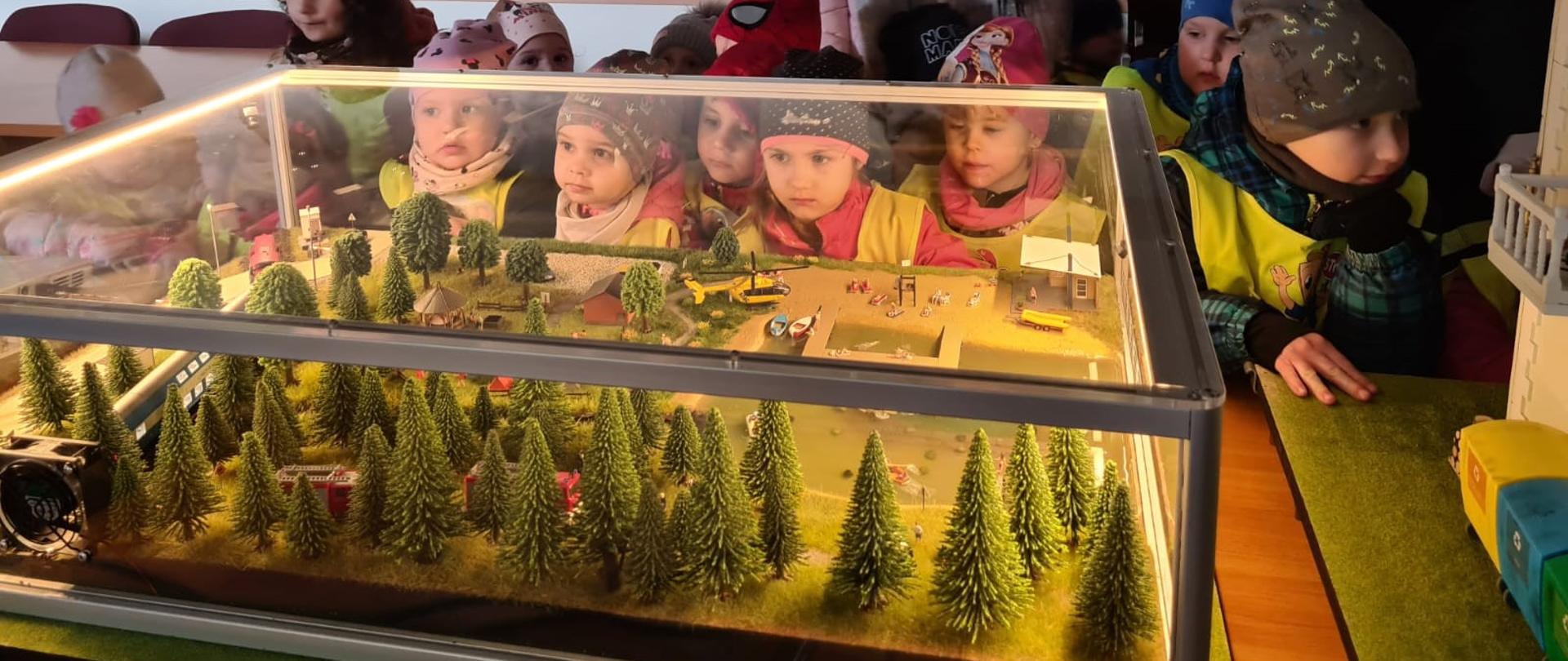 Makieta z lasem i jeziorem. W tle za szybą makiety widać grupę dzieci.