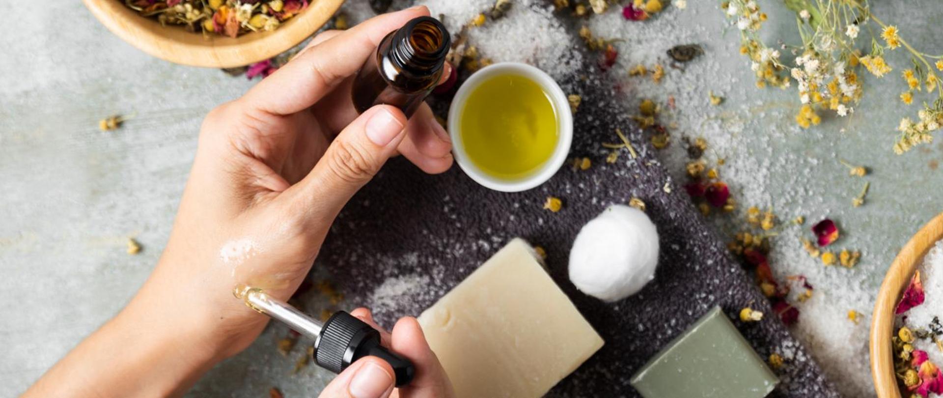 brązowa szklana buteleczka trzymana w lewej dłoni, w prawej dłoni trzymany zakraplacz w tle rozsypane drobne kwiatki