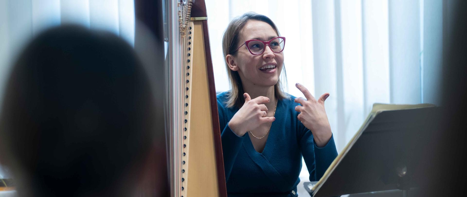 zdjęcie przedstawia wykładowcę przemawiającego i gestykulującego przy harfie w sali kameralnej