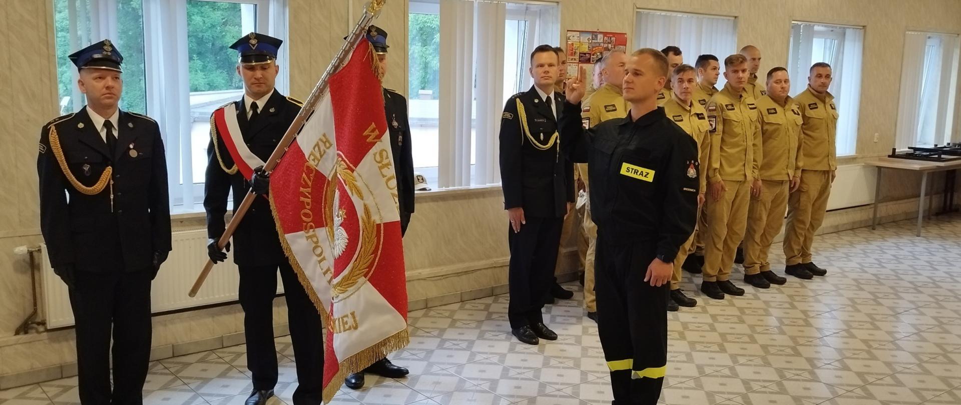 Zdjęcie przedstawia moment ślubowania złożonego przez strażaka Szymona Ciechowskiego. Przed nim poczet sztandarowy Komendy. Za ślubującym strażakiem funkcjonariusze podziału bojowego.