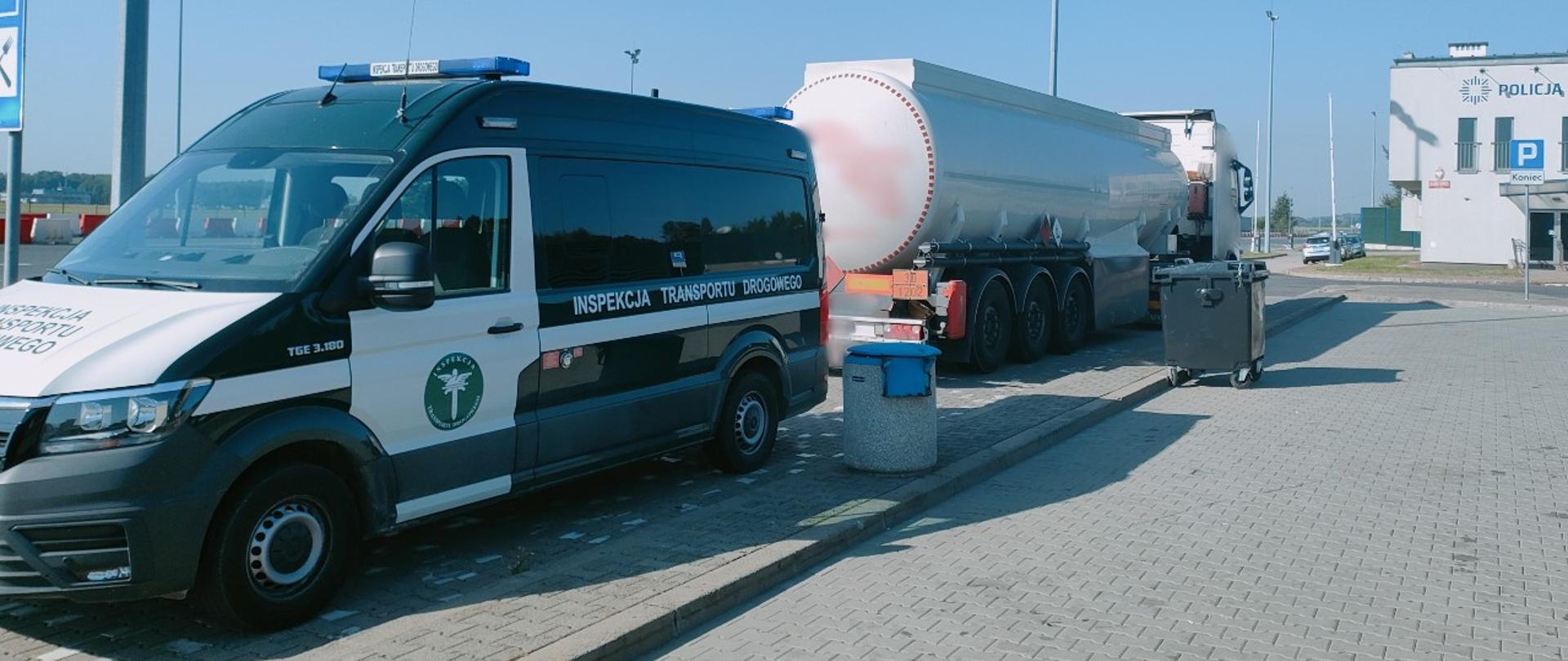 Na pierwszym planie (od lewej strony) przód i lewy bok oznakowanego furgonu małopolskiej ITD i stojący za nim zestaw ciężarowy z naczepą-cysterną przewożącą olej opałowy. W tle: budynek autostradowego posterunku Policji.