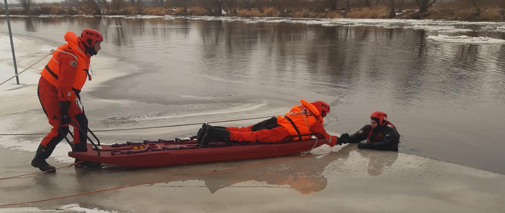 Strażacy na saniach wodno-lodowych podejmują osobę poszkodowaną z wody pod którą załamał się lód.