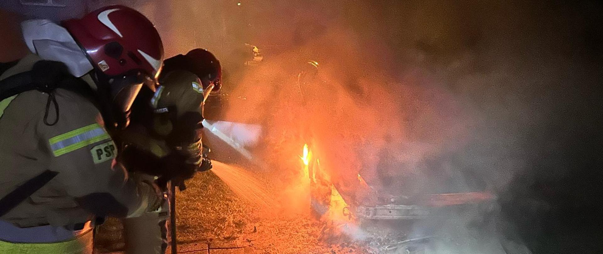 widoczne miejsce zdarzenia pojazd objęty pożarem oraz strażacy podczas podawania prądów gaśniczych