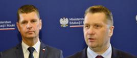 Minister Czarnek stoi i mówi do mikrofonu na stojaku, za nim wiceminister Piontkowski, za nimi niebieska ściana z napisem Ministerstwo Edukacji i Nauki.