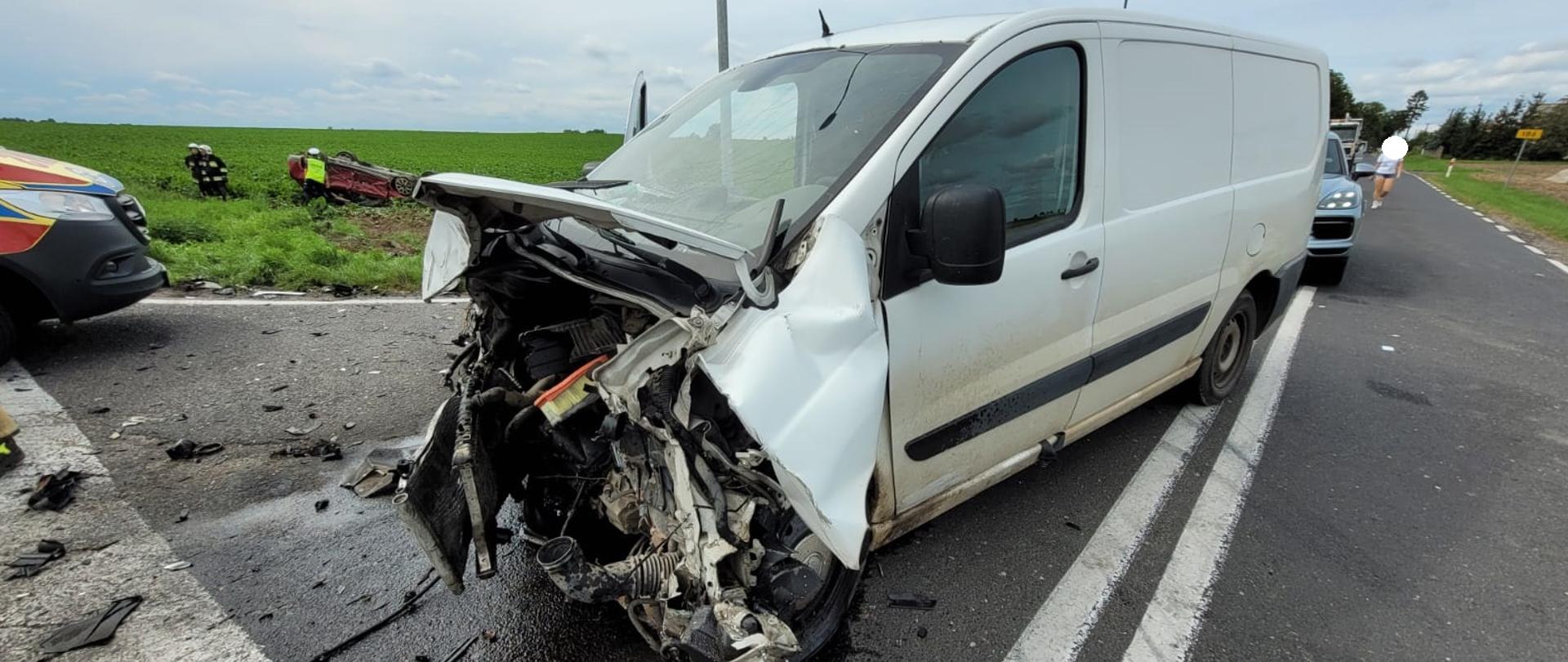 Biały samochód z uszkodzonym przodem znajduje się na środku skrzyżowania