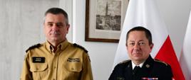 Pomorski komendant wojewódzki Państwowej Straży Pożarnej stoi ze strażakiem trzymającym list gratulacyjny.