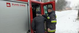 Na zdjęciu widnieje strażak Ochotniczej Straży Pożarnej pomagający przetransportować osobę starszą do punktu szczepień przeciwko COVID-19. 