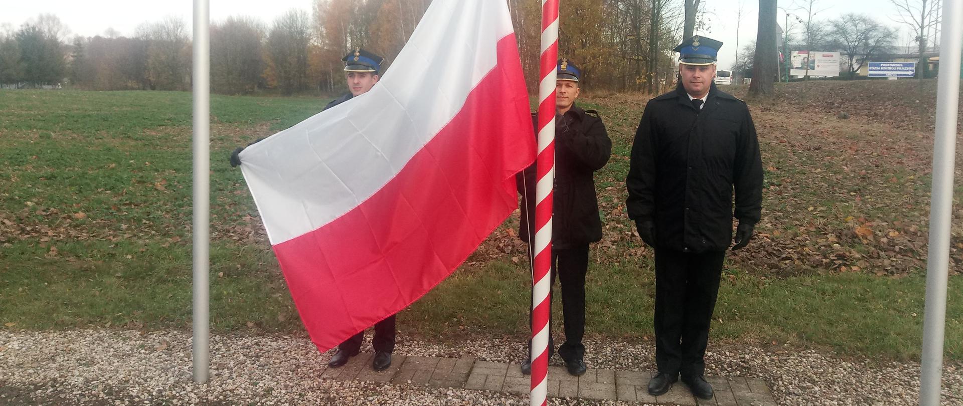 strażacy w mundurach wciągający flagę państwową na maszt
