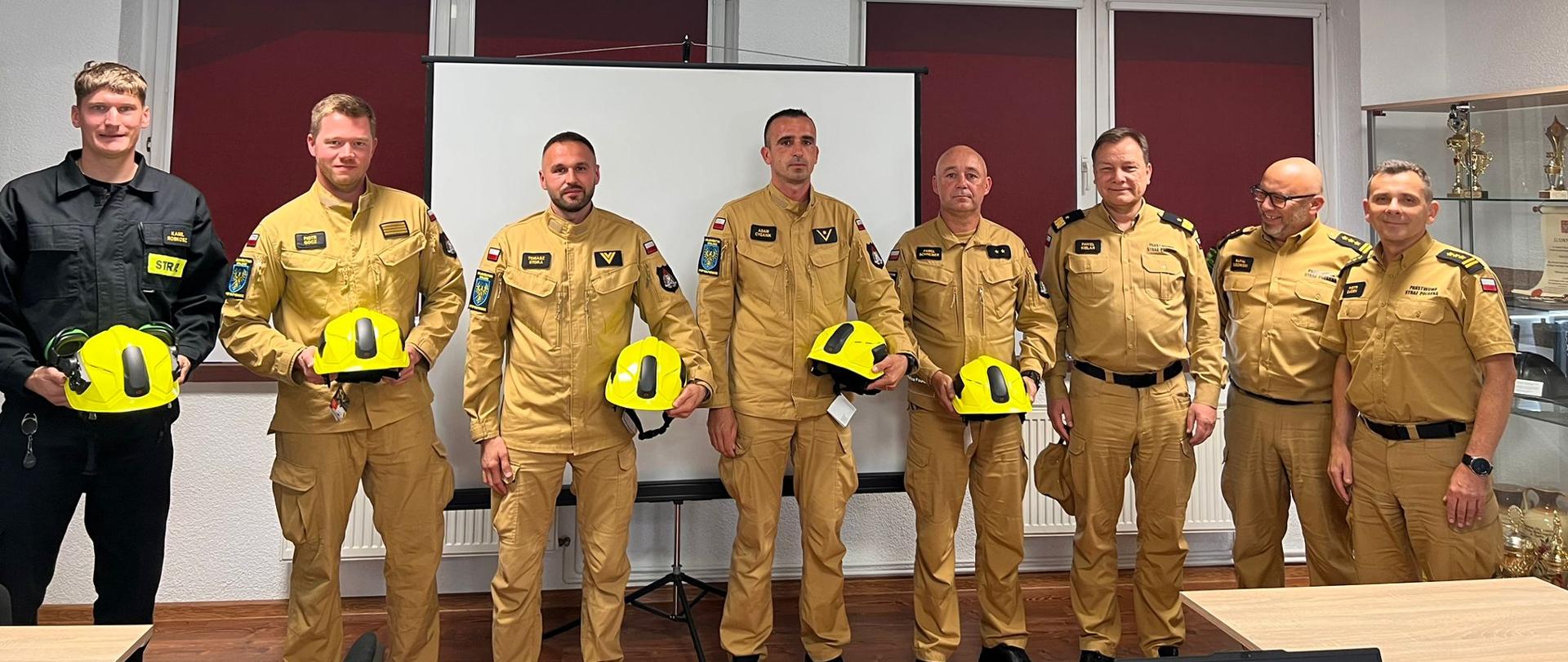 16 sierpnia 2025 roku w siedzibie Komendy Powiatowej Państwowej Straży Pożarnej w Krapkowicach, nadbryg. Paweł Kielar Opolski Komendant Wojewódzki PSP, st. bryg. Piotr Dudek Zastępca Opolskiego Komendanta Wojewódzkiego PSP oraz st. bryg. Rafał Bisowski Komendant Powiatowy PSP w Krapkowicach wraz ze st. bryg. Krzysztofem Muszyńskim Zastępcą Komendanta Powiatowego PSP w Krapkowicach spotkali się ze strażakami Jednostki Ratowniczo-Gaśniczej w Krapkowicach. Na spotkaniu obecni byli ponadto Naczelnicy Wydziału Planowania Operacyjnego oraz Ośrodka Szkolenia KW PSP w Opolu oraz funkcjonariusze KP PSP w Krapkowicach. Wspólne zdjęcie grupowe. Strażacy w umundurowaniu służbowym koloru piaskowego oraz koszarówkach koloru czarnego.