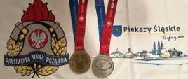 Zdjęcie przedstawia logotyp Państwowej Straży Pożarnej, medal brązowy i medal srebrny które zdobył młodszy aspirant Łukasz Żłobecki na Igrzyskach Służb Mundurowych w Birmingham w Stanach Zjednoczonych
