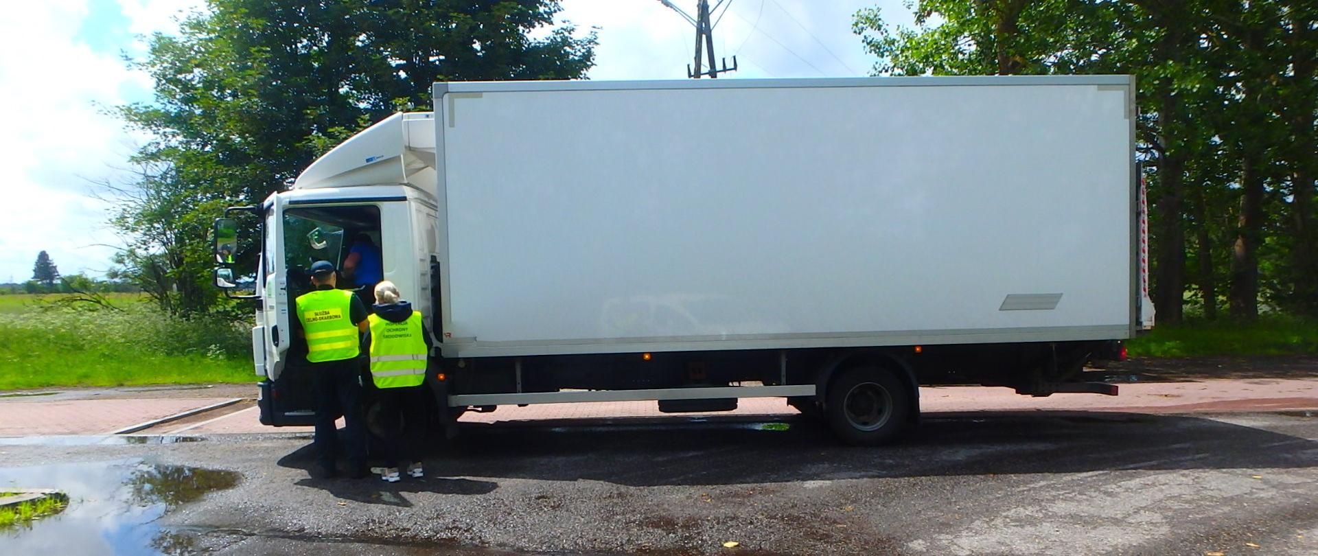 Przy zatrzymanej ciężarówce typu chłodnia inspektor WIOŚ w Gdańsku wraz z funkcjonariuszem Służby Celno-Skarbowej kontrolują dokumentację przewożonego ładunku.