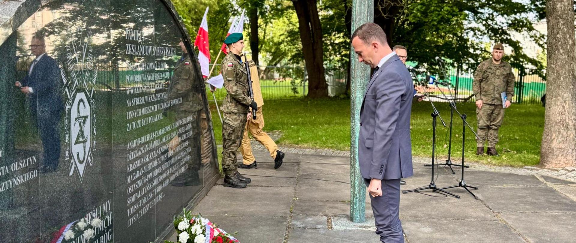 Mężczyzna stoi z głową pochyloną pod pomnikiem, pod którym jest wieniec 