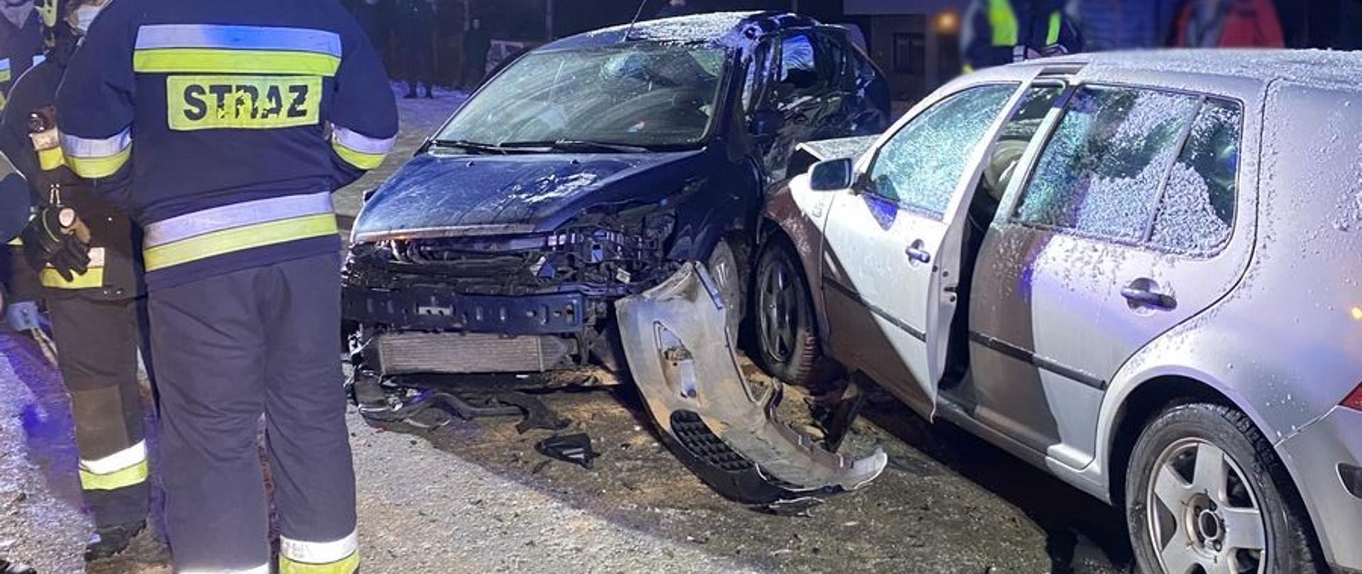 Dwa rozbite samochody osobowe a obok strażacy.