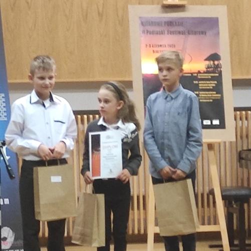 Zdjęcie trójki dzieci na scenie z upominkami w ręku.