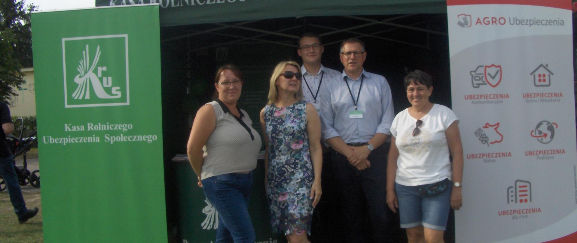 Trzy kobiety i dwóch mężczyzn przed stoiskiem w zielonym namiocie KRUS