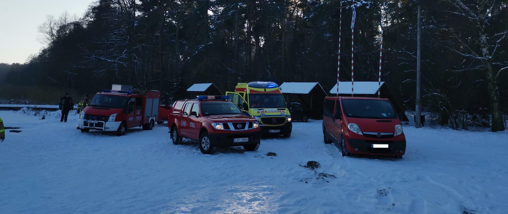 Samochody strażackie i karetka pogotowia na zaśnieżonej plaży.