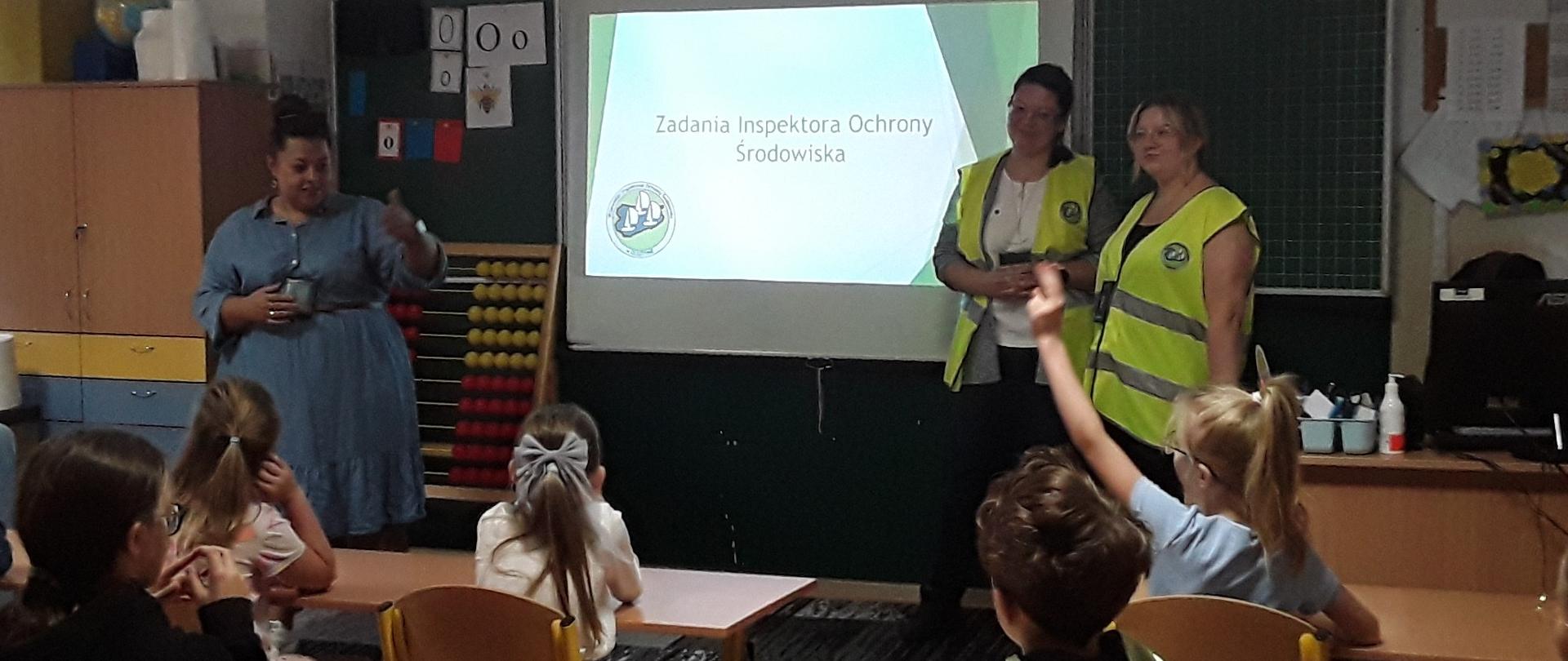 Inspektorki prezentują zagadnienia odpadowe. Po lewej stronie na dole logotyp Wojewódzki Inspektorat Ochrony Środowiska w Olsztynie. Z trzema łódkami na tle niebieskiego kształtu województwa warmińsko- mazurskiego.