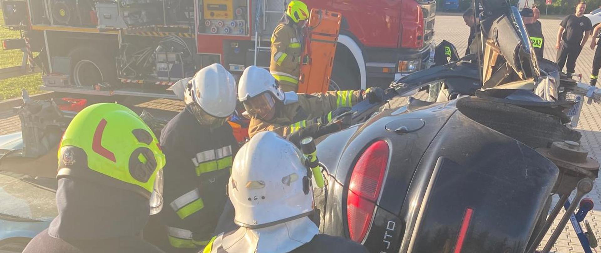 na zdjęciu strażacy w trakcie wykonywania zadania egzaminacyjnego,
w tle samochód pożarniczy