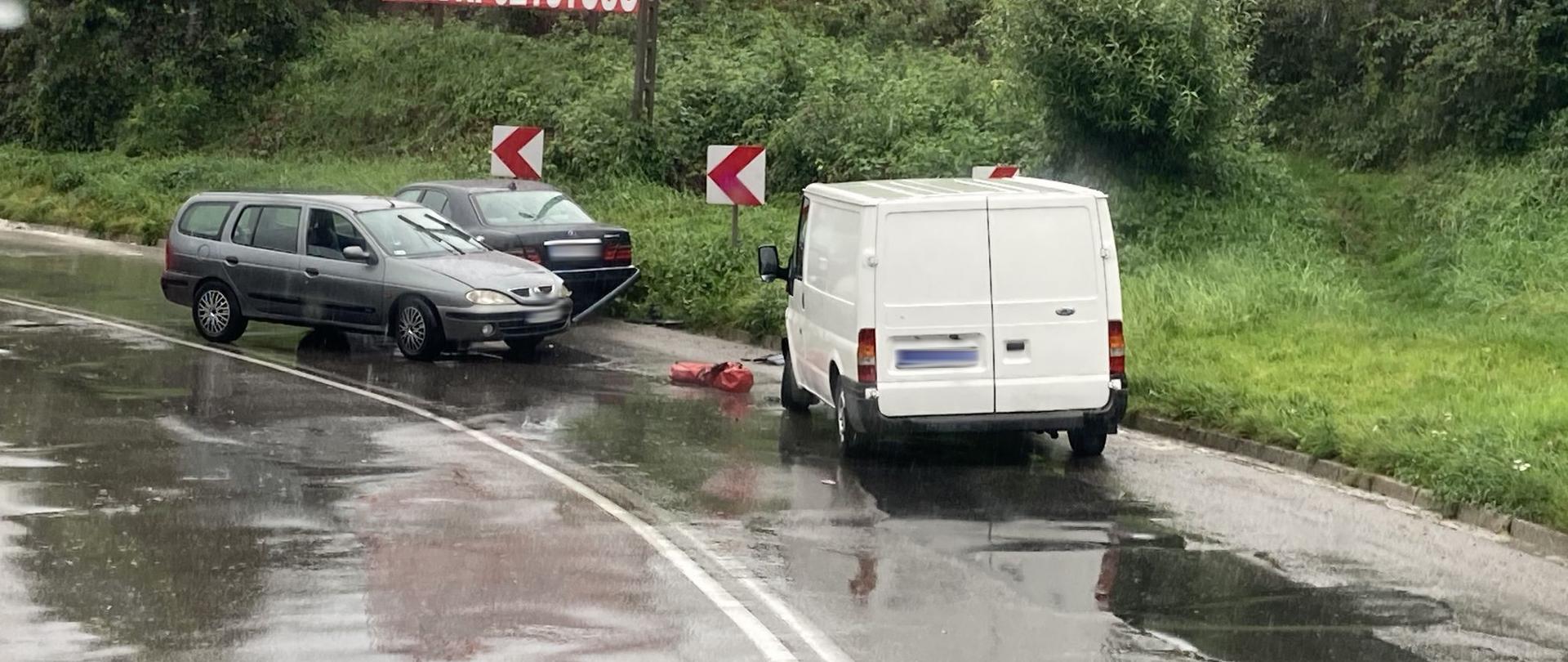 Trzy samochody uczestniczące w zdarzeniu na mokrej drodze.