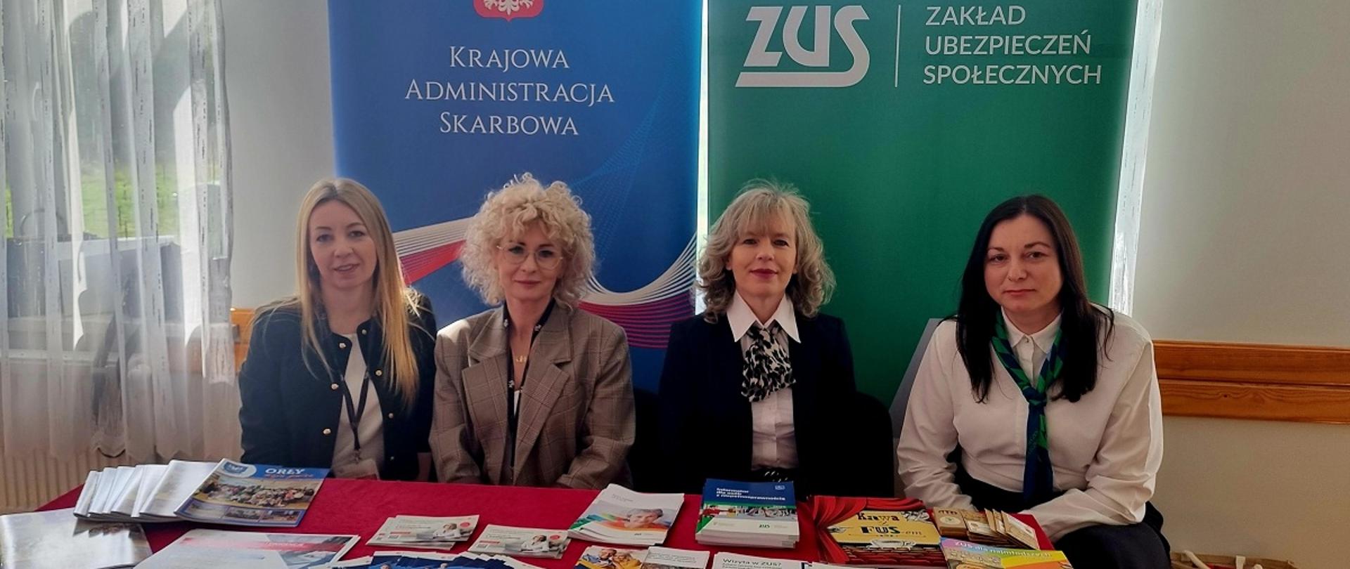 Przedstawicielki podkarpackiej KAS i ZUS siedzą przy stole. Na stole leżą ulotki. W tle baner KAS i ZUS.