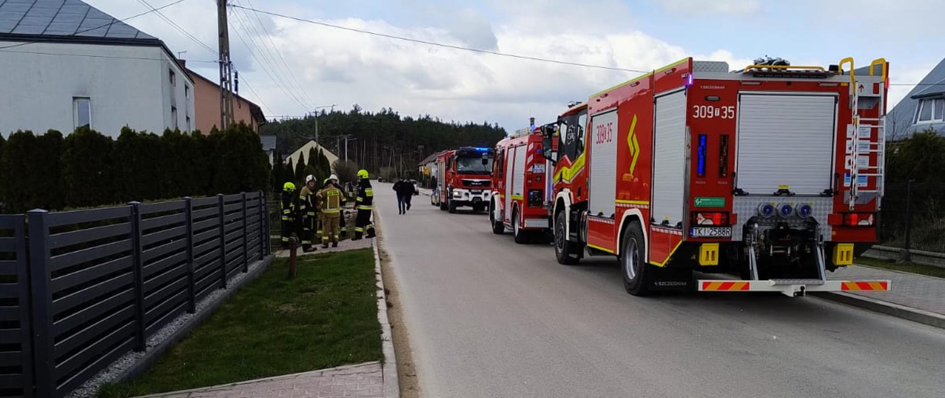Zdjęcie przedstawia miejsce samochody pożarnicze stojące wzdłuż drogi. Po lewej stronie widać budynek, w którym doszło do wybuchu.