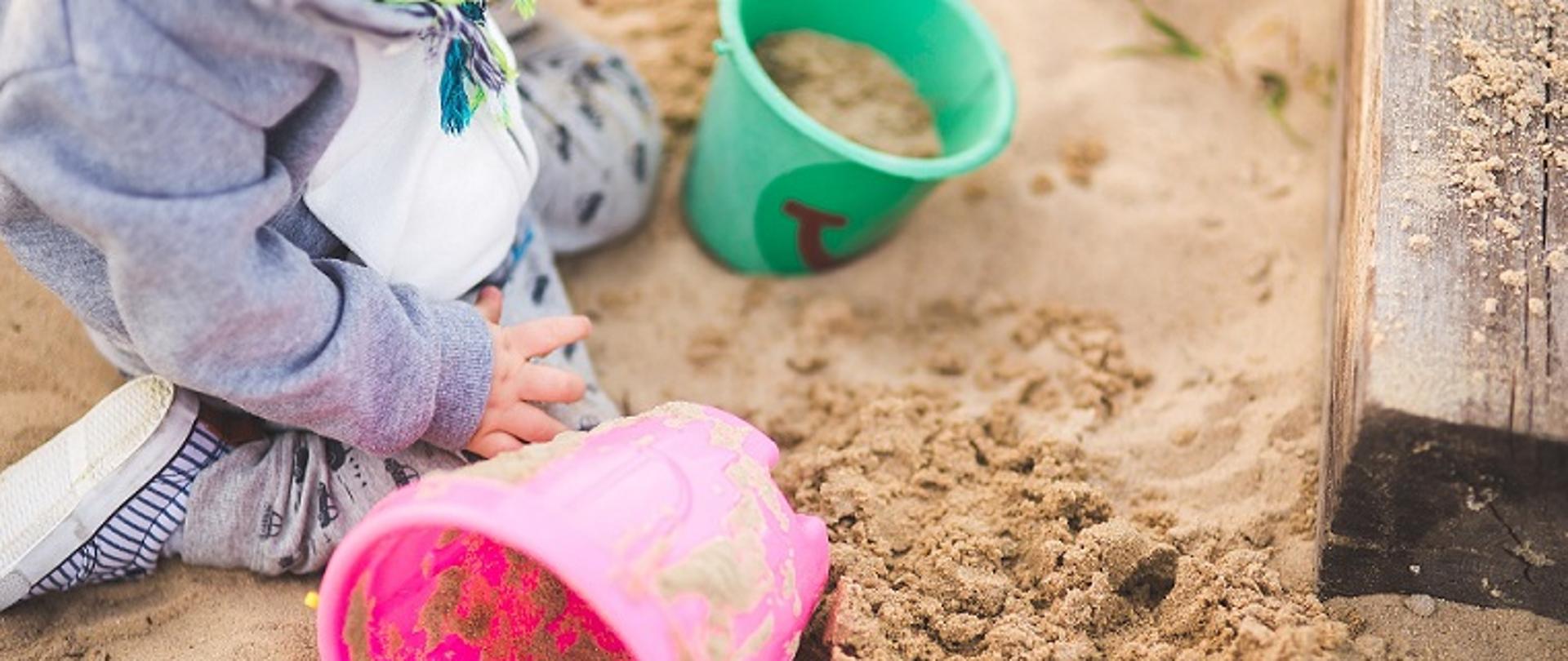 Małe dziecko w piaskownicy, bawi się piaskiem z wiaderkami