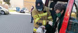 Strażak pomaga starszej kobiecie wysiąść ze strażackiego samochodu.