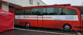 Zdjęcie przedstawia autokar Mobilny Punkt Poboru Krwi przed budynkiem KP PSP w Zduńskiej Woli. Z lewej strony stoi czerwony namiot z napisem Komenda Powiatowa Państwowej Straży Pożarnej w Zduńskiej Woli