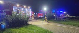 Zdjęcie przedstawia stojące samochody służb ratowniczych oraz strażaków wykonujących obowiazki słuzbowe.