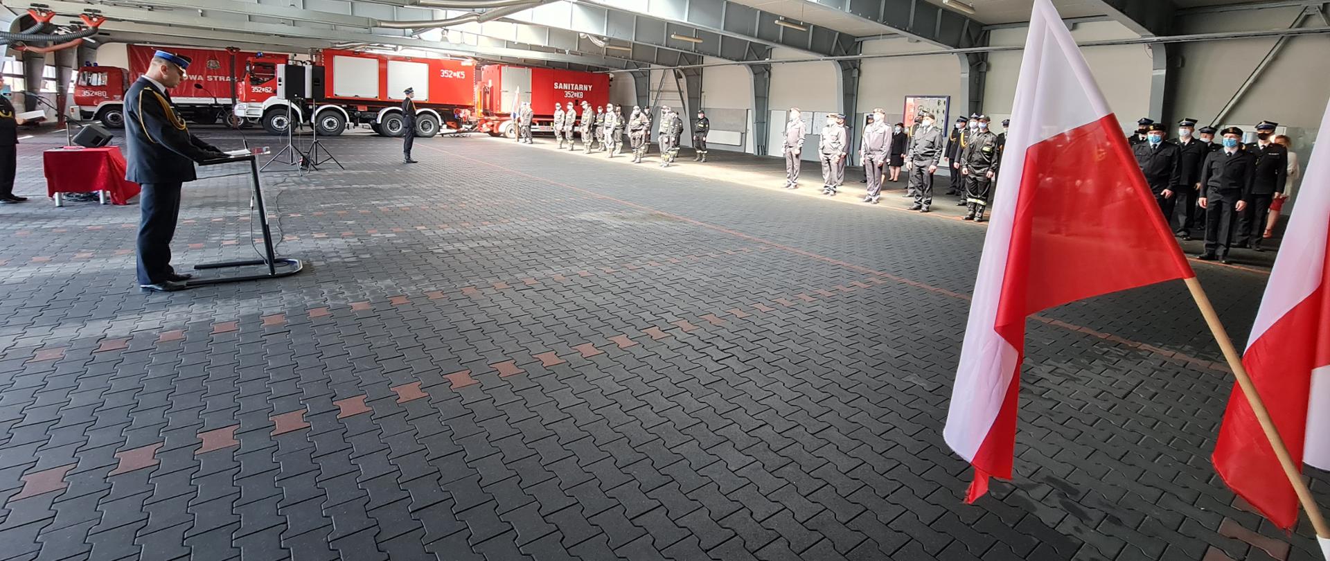 Zdjęcie przedstawia funkcjonariuszy i pracowników cywilnych podczas obchodów dnia strażaka. Na zdjęciu widać przemawiającego Komendanta miejskiego oraz pozostałych funkcjonariuszy podczas uroczystej zbiórki