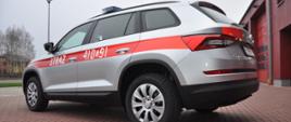 Na zdjęciu samochód lekki operacyjny marki Skoda Kodiaq na tle Komendy powiatowej PSP w Brzezinach. Samochód koloru srebrnego z oznaczeniami STRAŻ oraz numerem operacyjnym 410E91. Tył pojazdu
