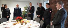 Na zdjęciu stoją zaproszeni goście, przedstawiciele władz samorządowych i zaprzyjaźnionych służb wokół zastawionego stołu. Zastępca Śląskiego Komendanta Wojewódzkiego st. bryg. Rafał Świerczek składa życzenia. 
