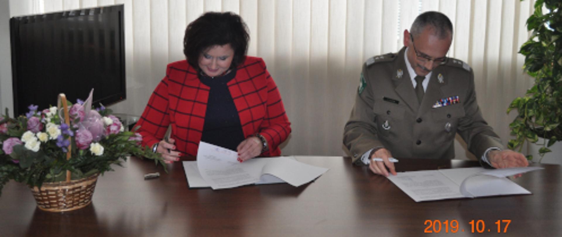 Na zdjęciu przy stole, na którym po lewej stronie stoi bukiet kwiatów siedzi Pani Małgorzata Zdrodowska Dyrektor Zakładu Emerytalno-Rentowego MSWiA , która podpisuje porozumienie o współpracy w obecności generała dywizji Straży Granicznej Tomasza Pragi, Komendanta Głównego Straży Granicznej .