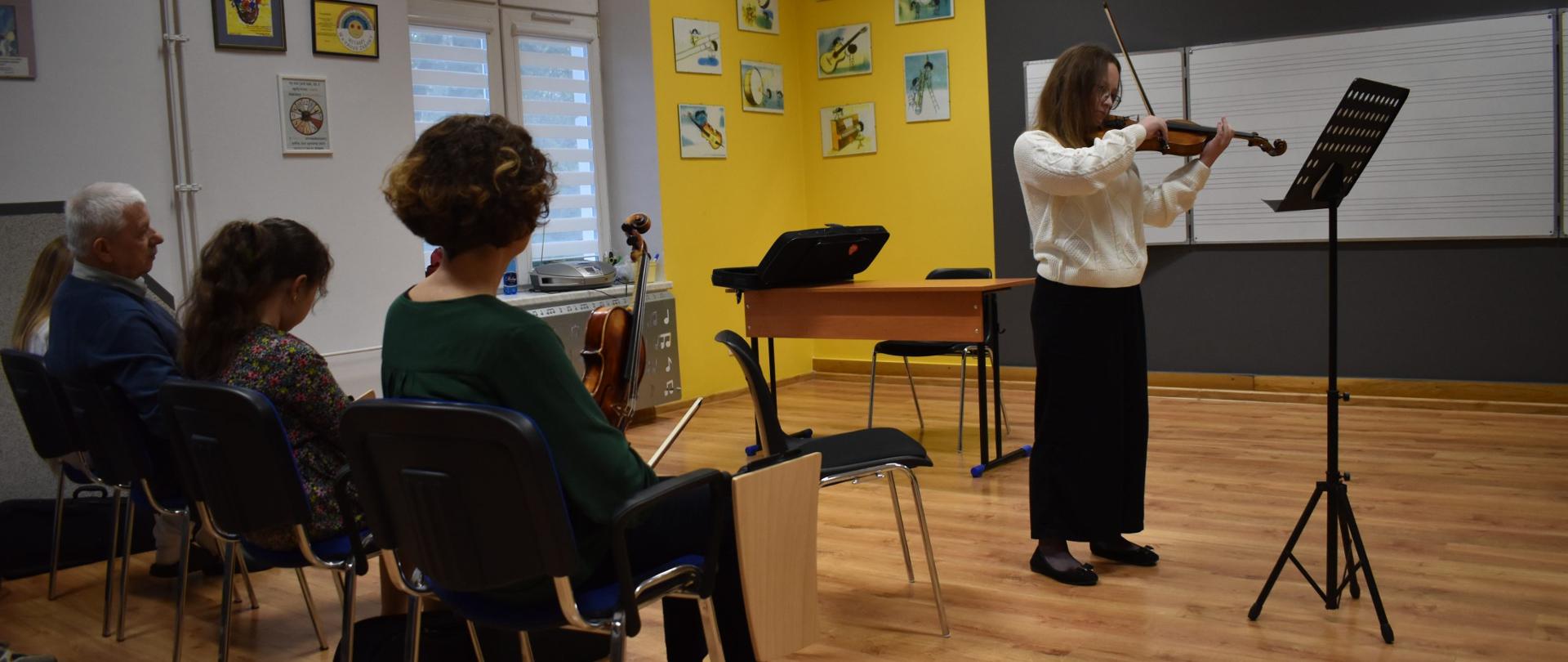 Na zdjęciu znajduje się pani Anna Śliwa i uczennica PSM I stopnia w Jaśle grająca na skrzypcach oraz nauczyciel i uczniowie słuchający występu 