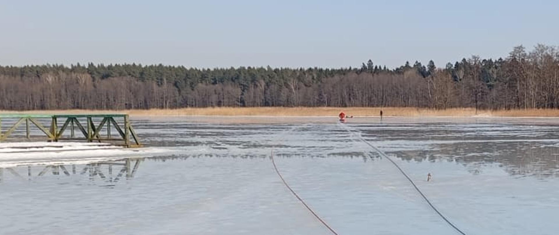 Zdjęcie przedstawia odpowiednio zabezpieczonych i wyposażonych ratowników Komendy Powiatowej Państwowej Straży Pożarnej w Gołdapi, którzy po dotarciu do osoby poszkodowanej udzielają mu pomocy