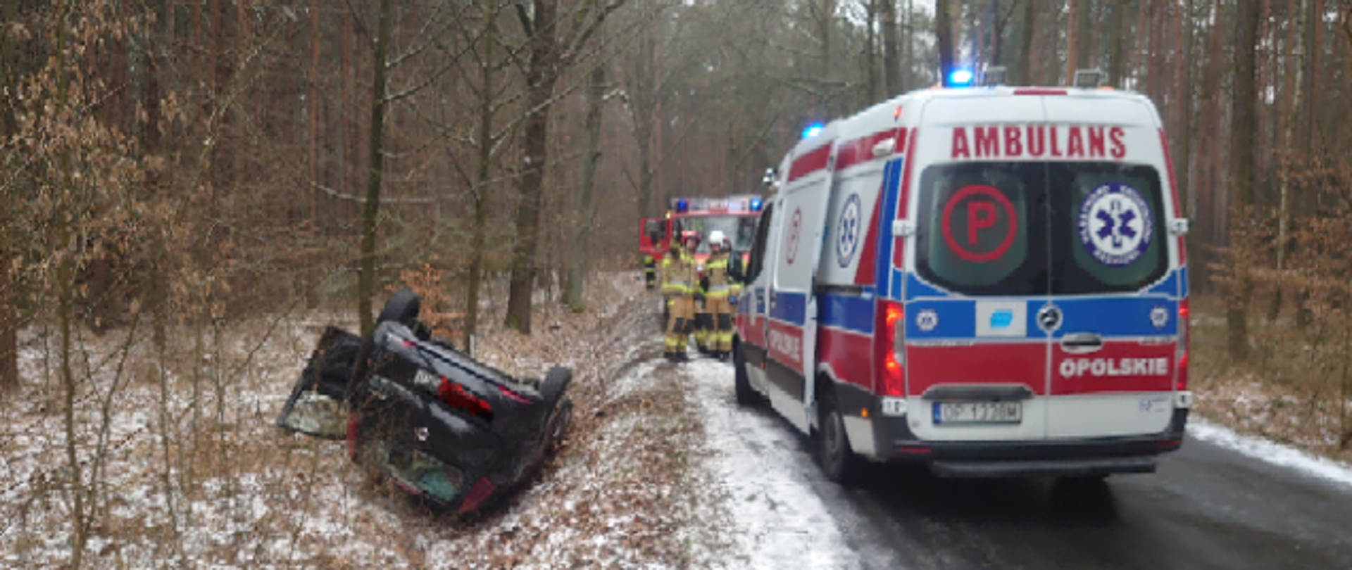 Na zdjęciu znajdują się strażacy, pojazdy pożarnicze, karetka pogotowia oraz wrak rozbitego samochodu na drodze
