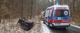 Na zdjęciu znajdują się strażacy, pojazdy pożarnicze, karetka pogotowia oraz wrak rozbitego samochodu na drodze