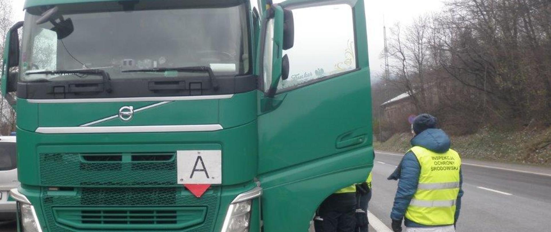 Pracownik Inspekcji Ochrony Środowiska oraz pracownicy Krajowej Administracji Skarbowej stojący przy otwartych drzwiach kontrolowanego samochodu ciężarowego.
