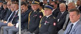 Zdjęcie przedstawia strażaków, parlamentarzystów, radnych oraz zaproszonych gości podczas uroczystości Obchodów Dnia Strażaka, którzy siedzą pod namiotem 