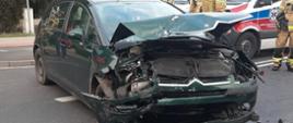 Zdjęcie przedstawia rozbity samochód osobowy marki Citroen C4 na tle karetki pogotowia.
