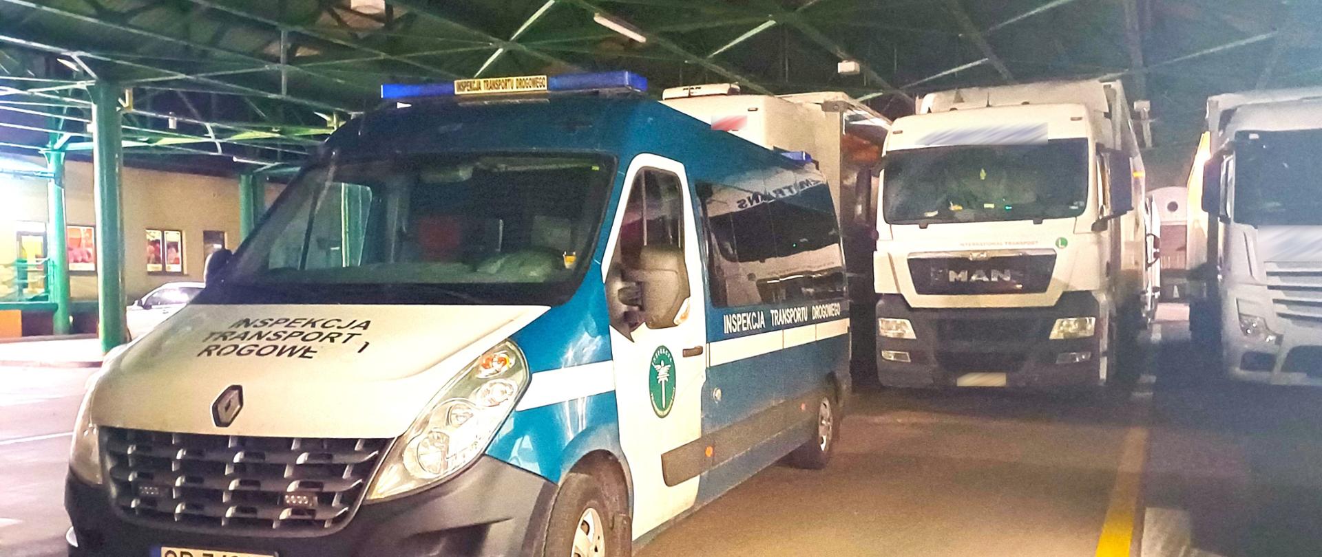 Opis alternatywny: Zdjęcie przedstawia pojazd Inspekcji Transportu Drogowego zaparkowany w zadaszonym miejscu kontroli drogowej. Za zielono-białym busem ITD stoją białe ciężarówki. Pojazdy ciężarowe zaparkowane są w jednej linii pod stalową konstrukcją dachu, w warunkach nocnych i przy sztucznym oświetleniu.