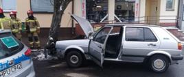 Na zdjęciu widać rozbity pojazd osobowy, a w tle radiowóz, strażaków oraz witryny sklepów 