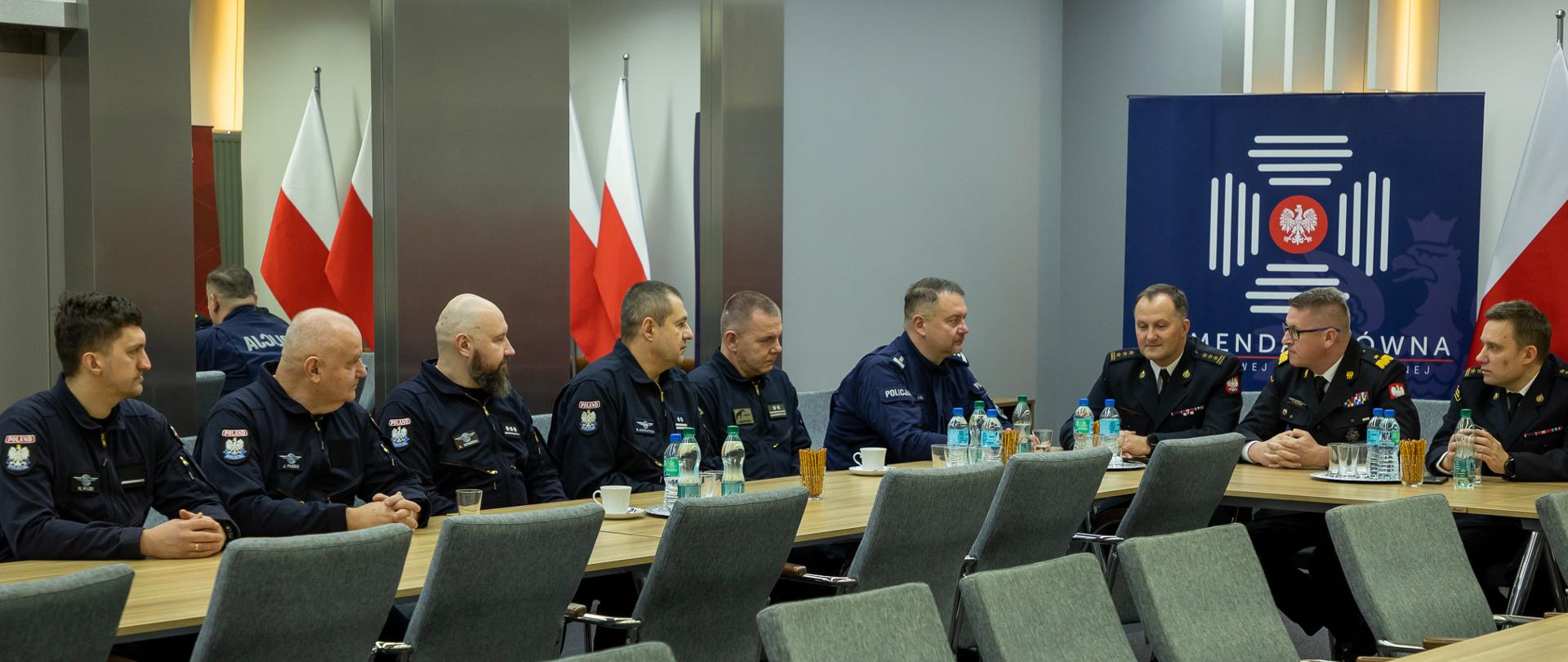 Na zdjęciu widać grupę Policjantów oraz strażaków podczas spotkania w sali konferencyjnej.