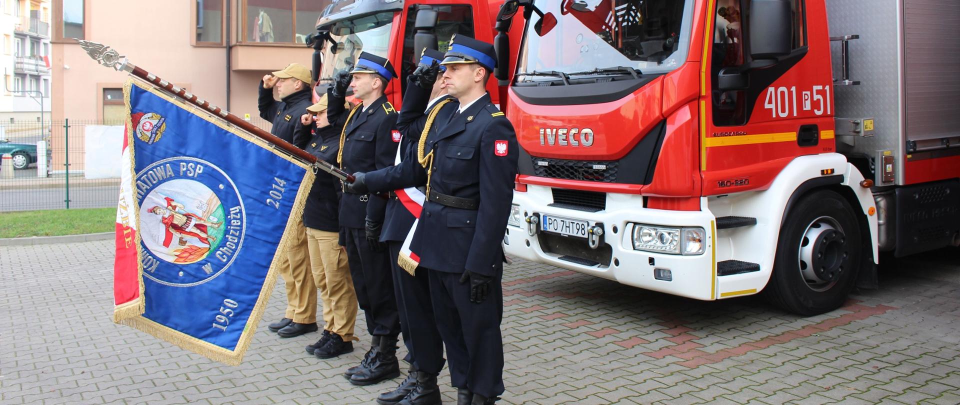 Zdjęcie przedstawia strażaków podczas uroczystości z okazji Święta Niepodległości.
W tle budynki.
