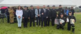 Męska drużyna ochotniczej straży pożarnej w Rogowie podczas gratulacji za zajęcie pierwszego miejsca. Chłopacy trzymają dyplom, puchar oraz zwycięskie nagrody.